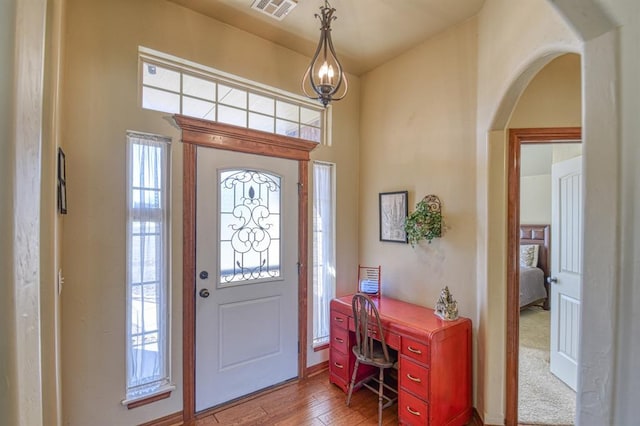 foyer entrance with wood finished floors, visible vents, a towering ceiling, and arched walkways