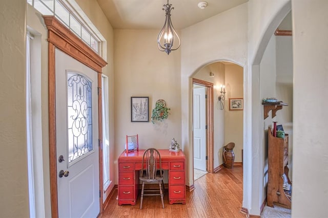 foyer with baseboards, arched walkways, and light wood finished floors