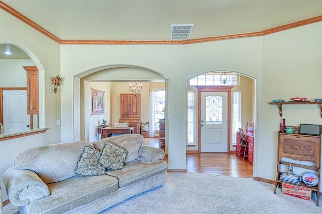 carpeted living room featuring visible vents, ornamental molding, arched walkways, an inviting chandelier, and baseboards