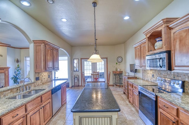 kitchen with a sink, backsplash, stainless steel appliances, arched walkways, and light stone countertops