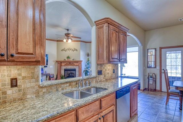 kitchen with dishwasher, light stone counters, arched walkways, a ceiling fan, and a sink