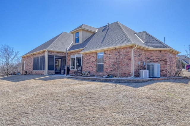 rear view of house with central AC unit, brick siding, a sunroom, and a shingled roof