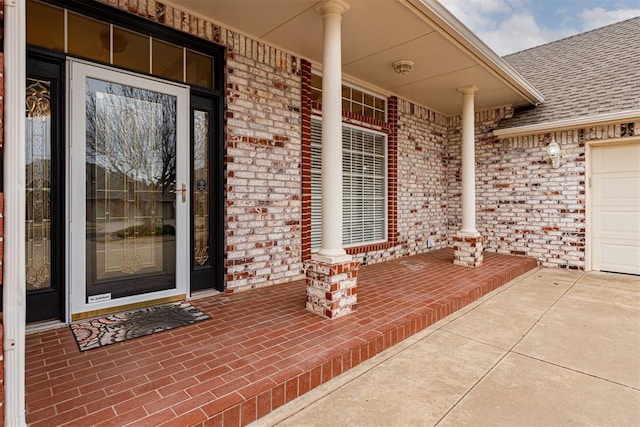 doorway to property with brick siding, a porch, an attached garage, and a shingled roof