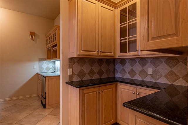 kitchen with tasteful backsplash, glass insert cabinets, dark stone counters, light tile patterned floors, and a sink