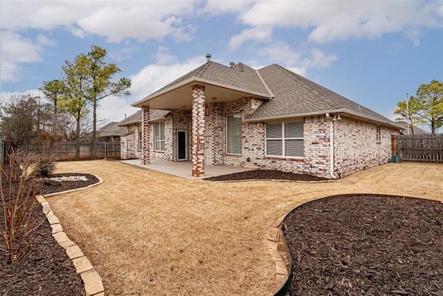 rear view of house featuring a patio area, brick siding, a fenced backyard, and a shingled roof