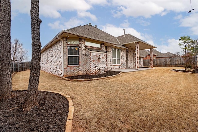 rear view of house with a fenced backyard, a shingled roof, a lawn, a patio area, and brick siding