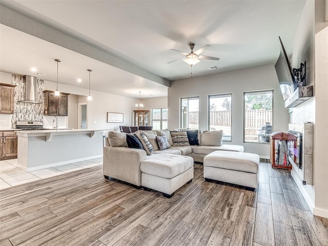 living room with visible vents, light wood finished floors, baseboards, and ceiling fan with notable chandelier