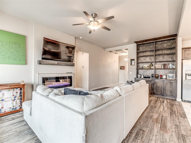 living area with a glass covered fireplace, a ceiling fan, and light wood finished floors