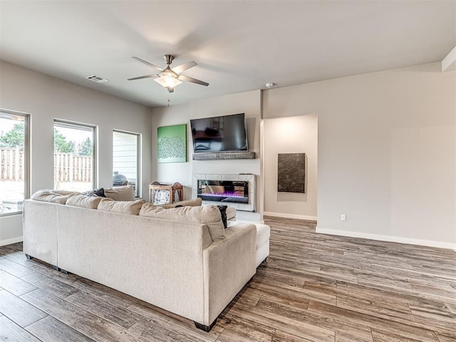 living area with visible vents, baseboards, ceiling fan, wood finished floors, and a glass covered fireplace