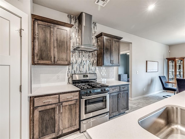 kitchen featuring tasteful backsplash, baseboards, wall chimney range hood, light countertops, and gas stove