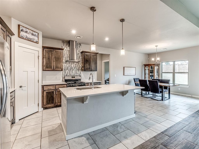 kitchen featuring a sink, wall chimney range hood, stainless steel range with gas cooktop, light countertops, and decorative backsplash