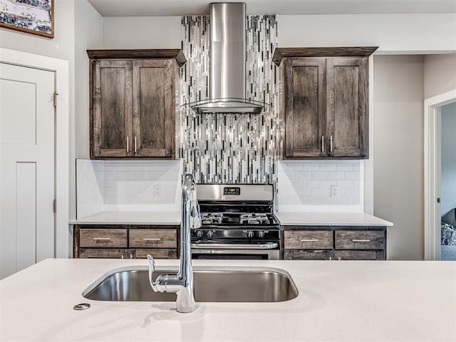 kitchen featuring stainless steel range with gas cooktop, a sink, light countertops, dark brown cabinetry, and wall chimney range hood