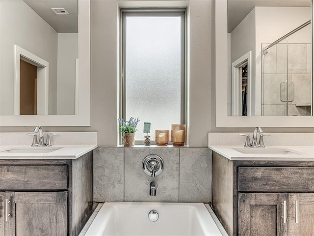 full bath featuring two vanities, a bath, visible vents, and a sink