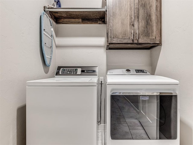 laundry area with a textured wall, cabinet space, and washer and clothes dryer