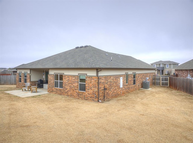 back of house featuring roof with shingles, a fenced backyard, central AC, a patio area, and brick siding