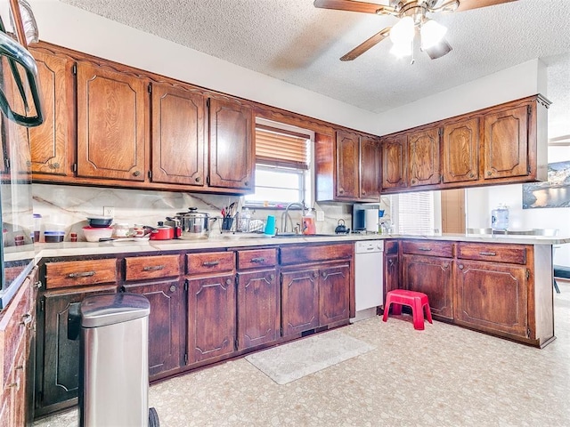 kitchen with a ceiling fan, a sink, a textured ceiling, a peninsula, and white dishwasher