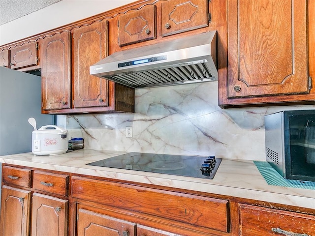 kitchen with brown cabinets, under cabinet range hood, tasteful backsplash, light countertops, and black electric cooktop