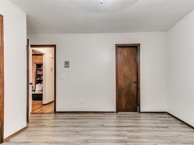 unfurnished room with baseboards, a textured ceiling, and light wood-style floors