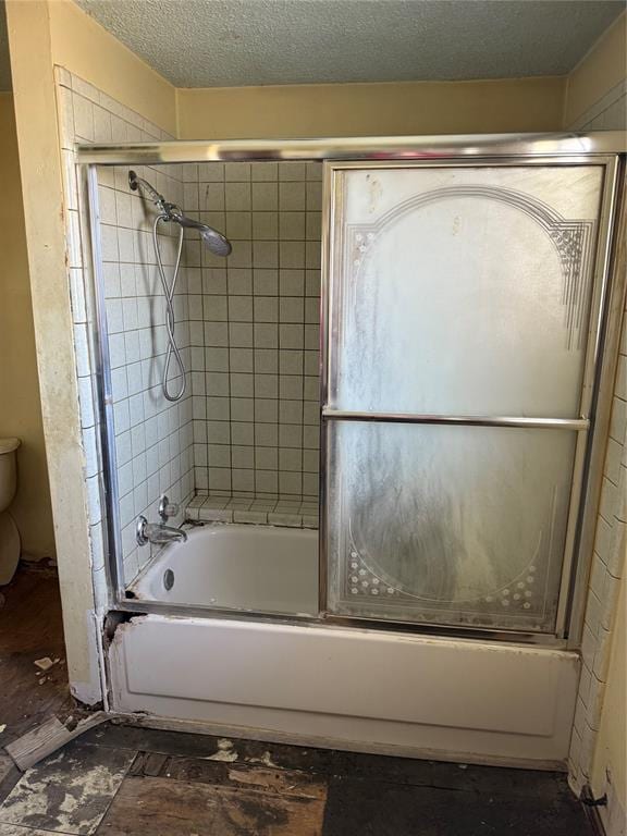 bathroom featuring toilet, bath / shower combo with glass door, and a textured ceiling