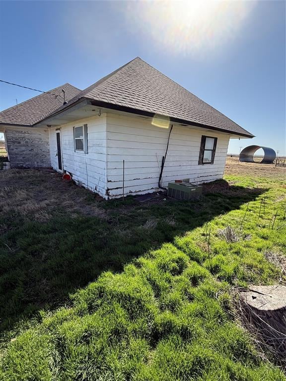 view of side of property featuring a lawn and roof with shingles