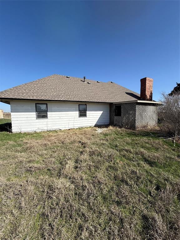 rear view of house featuring a lawn, roof with shingles, and a chimney