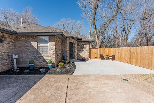 exterior space featuring a gate, fence, brick siding, and a shingled roof