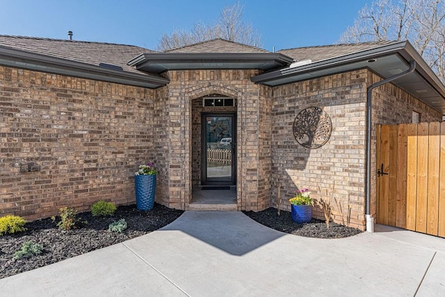 view of exterior entry featuring brick siding and roof with shingles