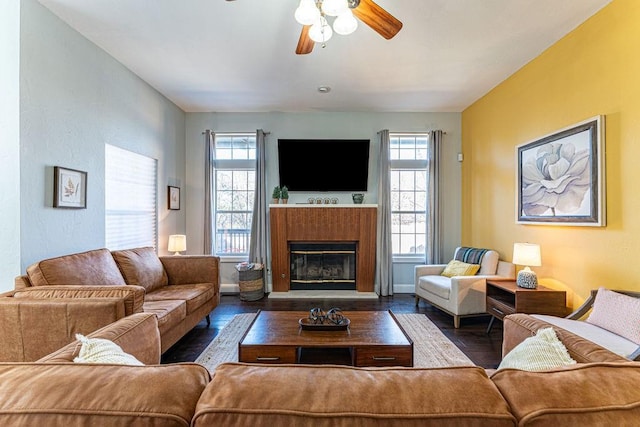 living area with a glass covered fireplace, wood finished floors, baseboards, and ceiling fan