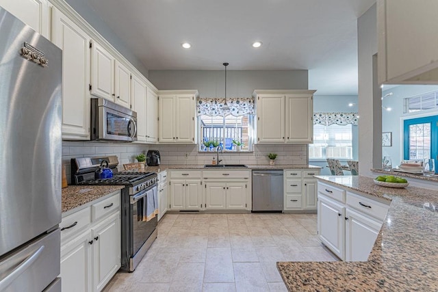 kitchen featuring tasteful backsplash, light stone counters, stainless steel appliances, white cabinetry, and a sink