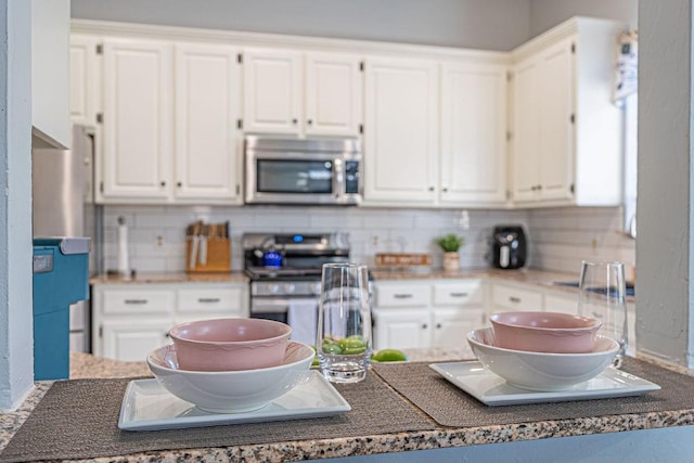 kitchen with dark countertops, tasteful backsplash, appliances with stainless steel finishes, and white cabinetry