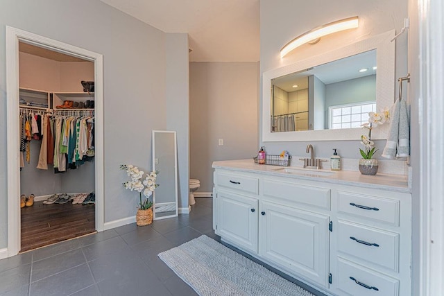 bathroom with tile patterned floors, a walk in closet, toilet, baseboards, and vanity