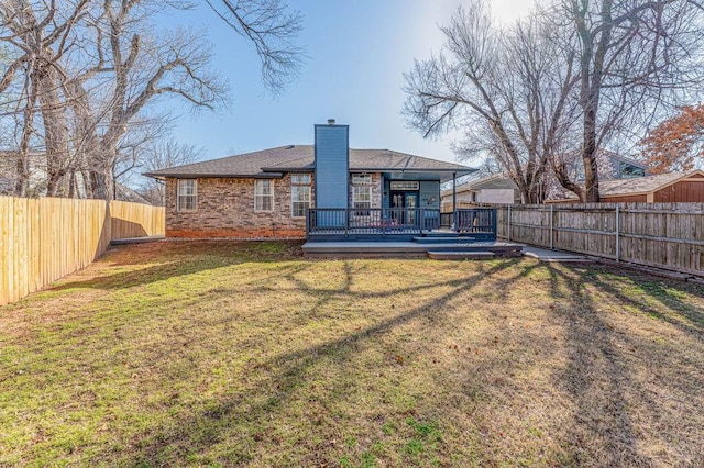 rear view of house with a deck, a lawn, a chimney, and a fenced backyard