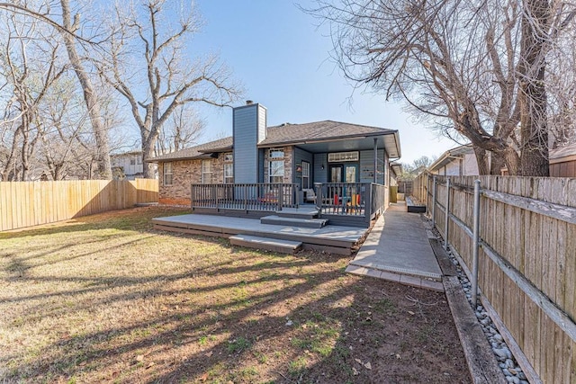 rear view of property with a yard, a deck, a fenced backyard, and a chimney