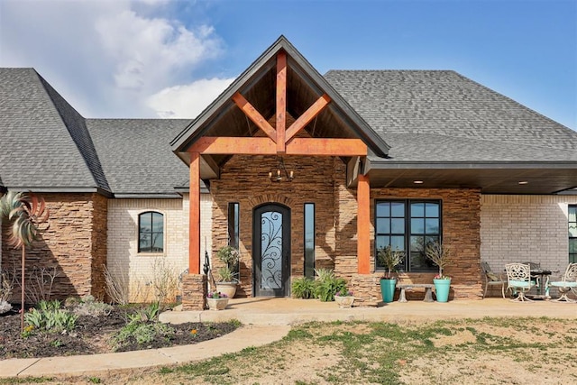 view of front of house with a shingled roof, brick siding, and stone siding