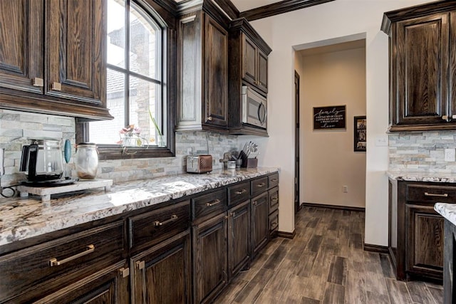 kitchen with stainless steel microwave, light stone countertops, dark brown cabinets, tasteful backsplash, and dark wood-style flooring