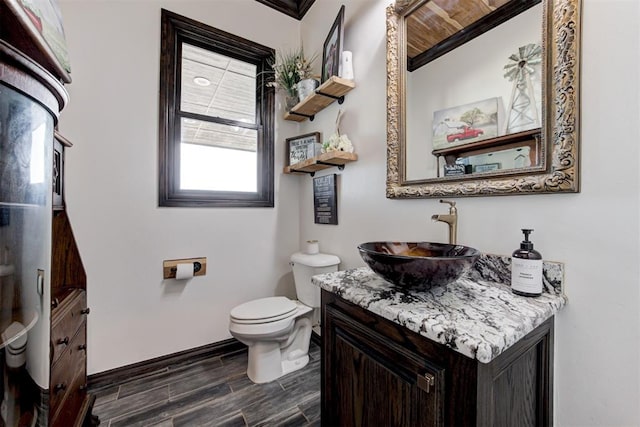 half bath featuring toilet, baseboards, wood finished floors, vanity, and crown molding