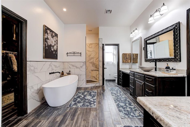 full bath featuring tile walls, a tile shower, vanity, a freestanding bath, and toilet