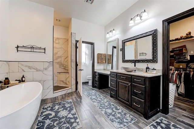 full bathroom featuring a tile shower, toilet, vanity, a soaking tub, and wood finish floors