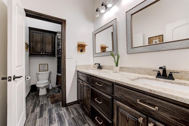 bathroom with toilet, double vanity, wood finish floors, and baseboards