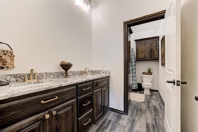 bathroom featuring toilet, wood finished floors, baseboards, and double vanity