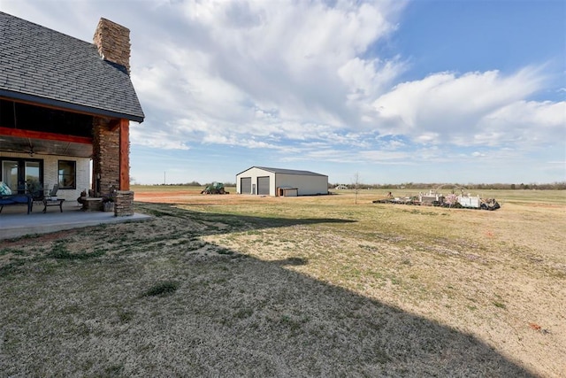 view of green lawn featuring a garage, a patio, a view of countryside, and an outbuilding