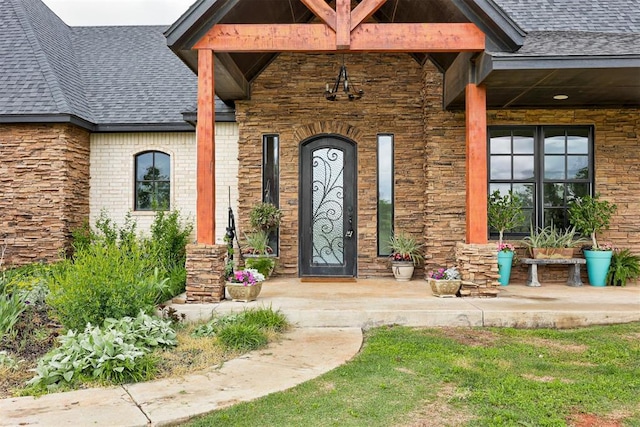entrance to property with a shingled roof, a porch, and brick siding
