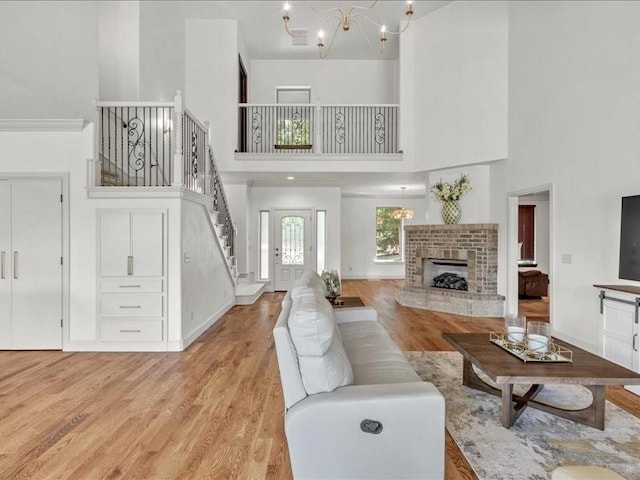 living room with stairs, light wood finished floors, a fireplace, a high ceiling, and an inviting chandelier