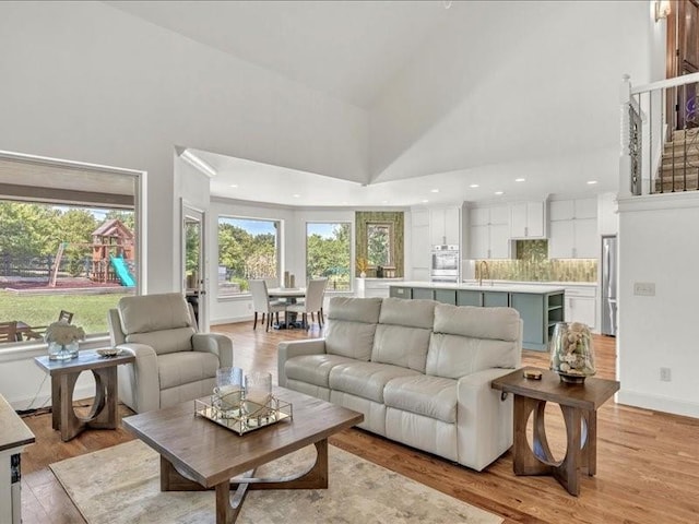 living area with light wood-style flooring, high vaulted ceiling, and baseboards