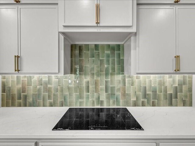 kitchen featuring white cabinets, black electric stovetop, backsplash, and light stone countertops