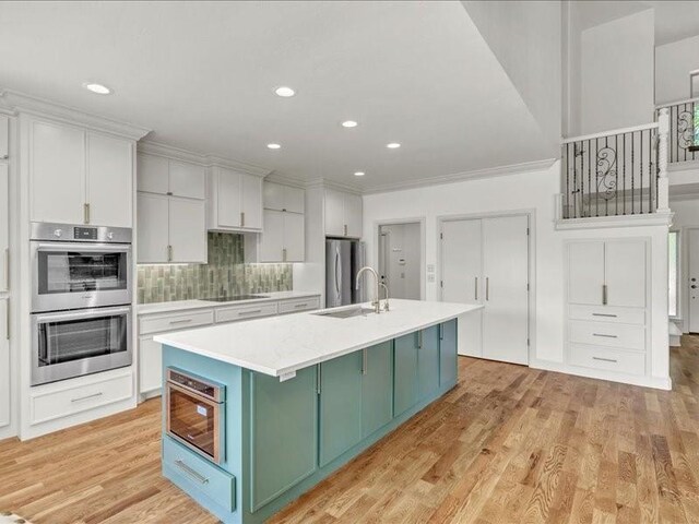 kitchen featuring light countertops, stainless steel appliances, a sink, green cabinetry, and light wood-type flooring