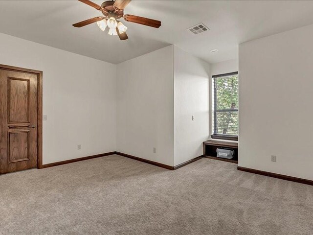 carpeted empty room with baseboards, ceiling fan, and visible vents