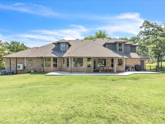 rear view of property featuring roof with shingles, a patio, fence, brick siding, and a lawn