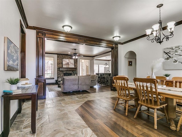 dining area featuring arched walkways, wood finished floors, a fireplace, and crown molding