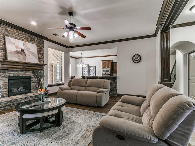 living room with baseboards, ornamental molding, a stone fireplace, wood finished floors, and a ceiling fan